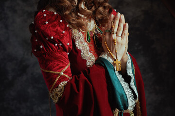 Closeup on medieval queen in red dress with rosary praying