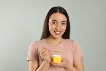 Poster - Portrait of happy woman with tasty yogurt on grey background