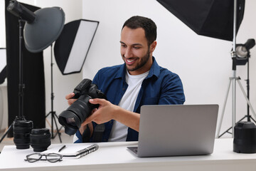 Poster - Young professional photographer with camera at table in modern photo studio