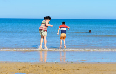 mother and son jumping in the sea water near beach in summer