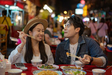 Young Asian Couple Traveler Tourists Eating Thai Street Food Together In China Town Night Market In Bangkok In Thailand - People Traveling Enjoying Food Culture Concept