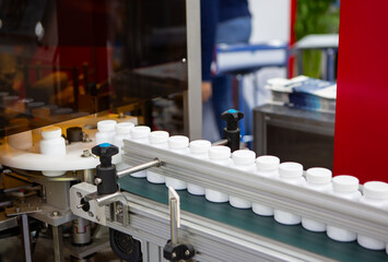 Wall Mural - White plastic bottle on capsule filling machine conveyor belt in production line. Pharmaceutical industry	
