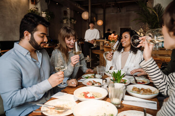 Wall Mural - Group of friends enjoying delicious meal and wine while sitting in restaurant