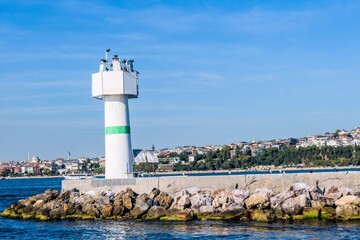 White lighthouse on concrete pier in Bosporus Strait with Istanbul city in background.