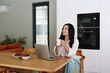 © Westend61 - Thoughtful woman holding coffee cup sitting with laptop at table at home