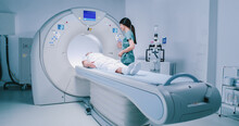 Patient Is Getting Recommendations From Doctor Before MRI Procedure. Woman Is Lying Down At CT Scanner Bed. Female Is Moving Into MRI Scanner Capsule. Female Doctor Is Conducting Tomography Examining.
