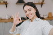 © ViDi Studio - Close up smiling fun young happy housewife latin woman wear casual clothes shirt doing selfie shot pov on mobile cell phone sit at table in light kitchen at home alone. Lifestyle cooking food concept.