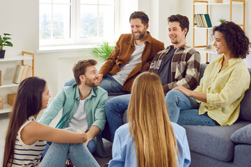 Wall Mural - Group of a happy young friends men and women sitting in the living room at home talking with each other, laughing at joke enjoying meeting. Friendship, party and home leisure concept.