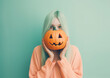 A girl wearing a pumpkin mask for Halloween in front of a pink pastel background. Generative AI