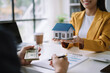 © NINENII - Real estate broker agent presenting and consult to customer to decision making sign insurance form agreement, home model, concerning mortgage loan offer.
