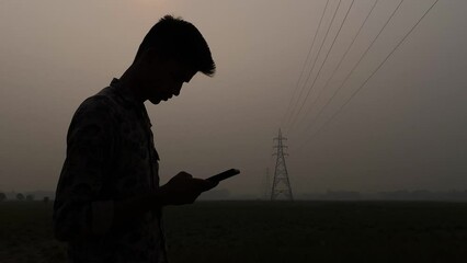 a young south asian boy is using a smartphone in the evening. a black figure using a cell phone and 