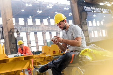 Steel worker texting with cell phone taking a break in factory