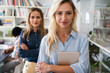 © NDABCREATIVITY - Two happy successful business female collegues standing next to each other in an office