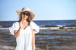 © rogerphoto - Happy blonde woman is posing on the ocean beach with sunglasses and a hat. Evening sun