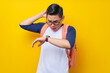 © Bangun Stock Photo - Worried and shocked young Asian man student in casual clothes and glasses backpack scratching head and raising hand, looking watch isolated on yellow background. high school university college concept