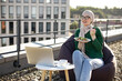 Smiling arabian woman in headscarf and eyewear having snack while doing outdoor office work on flat roof of building. Cheerful business lady enjoying healthy food while thinking over startup project.
