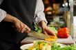 © AnnaStills - Close-up of hands of young female kitchen worker chopping fresh yellow pepper for salad or some other dish while standing by workplace