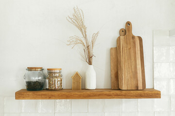 Wooden shelf with rustic cutting board, tea jar and decor in modern kitchen in new scandinavian house. Modern kitchen interior and stylish farmhouse utensils