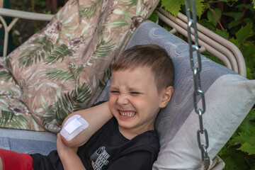 preschool boy hurt. he sits on a bench with a medical patch on his elbow in the backyard and cries