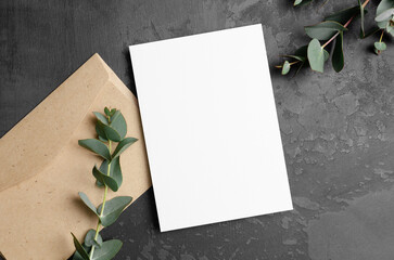 Invitation or greeting card mockup with fresh eucalyptus twigs and envelope on dark background