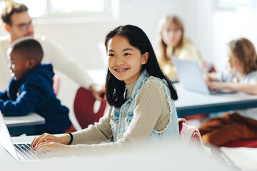 Wall Mural - Happy Asian girl enjoying a coding class, using a laptop to engage in the lesson