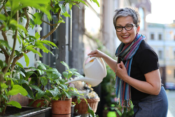 Poster - Stylish adult woman watering flowers in a flower bed near a flower shop.