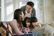 happy young asian family with two children sitting on couch at home using notebook computer together