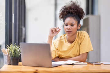 Wall Mural - Business And Education Concept. Smiling african american  sitting at desk working on laptop writing letter in paper documents, free copy space. Happy millennial female studying using laptop	