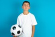 Little hispanic boy wearing white T-shirt holding a football ball looking sleepy and tired, exhausted for fatigue and hangover, lazy eyes in the morning.