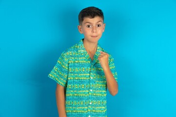 Little hispanic boy wearing green aztec shirt shows fist has annoyed face expression going to revenge or threaten someone makes serious look. I will show you who is boss