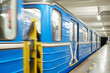 Perspective view of long blue subway train with people inside moving with high speed along empty platform and illuminated metro tunnel