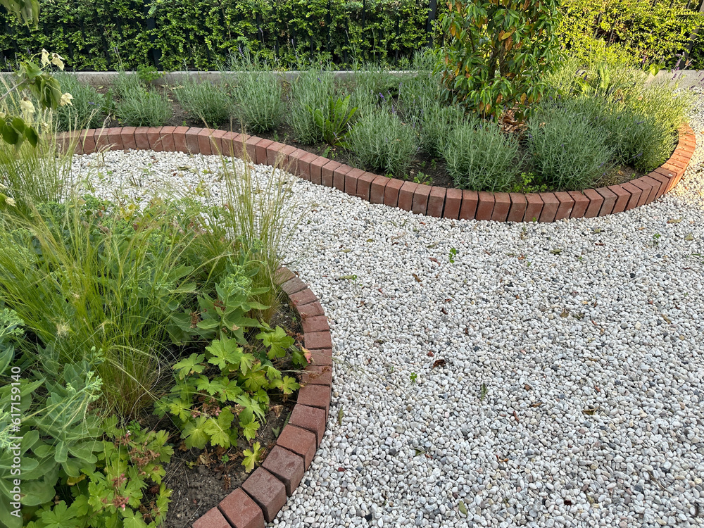 Stone pathway in the garden. Fragment of front garden with grey gravel. Flower beds and brick borders
