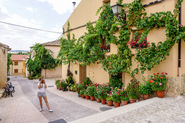 Beautiful young woman with blonde hair taking photos with her cell phone on a street decorated with plants