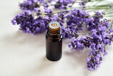 Fototapeta Lawenda - A dropper bottle of essential oil with blooming lavender plant on a white table