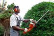 © Богдан Маліцький - garden worker in uniform cuts bushes, african american man in goggles and headphones works in the garden
