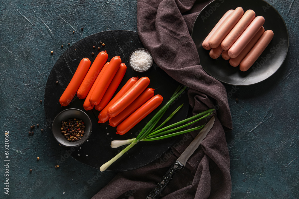 Plate and board with tasty thin sausages on dark background