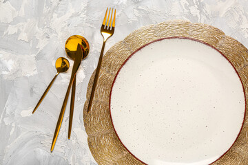 Place mat with clean plate and set of golden cutlery on grey grunge table