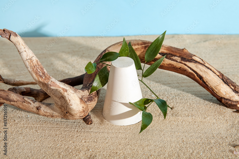 Decorative plaster podium and branch with leaves on sand against blue background