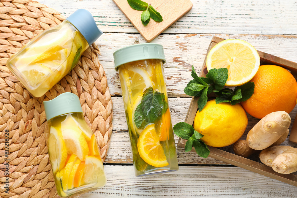 Sports bottles of infused water and box with different citrus fruits on white wooden background