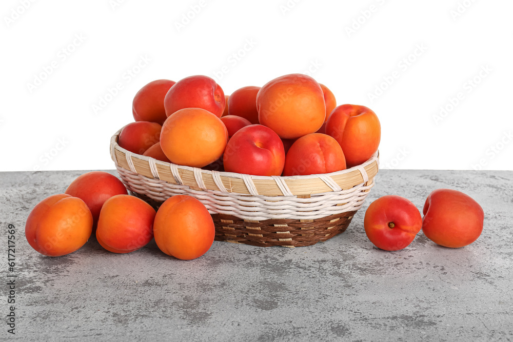 Wicker basket with ripe apricots on table against white background