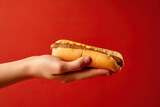 Fototapeta Tęcza - Hand holding tasty hot dog on a red background