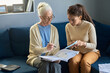 © AnnaStills - Youthful multiethnic girl with small paper and her grandmother looking at payment document or financial bill while comparing information