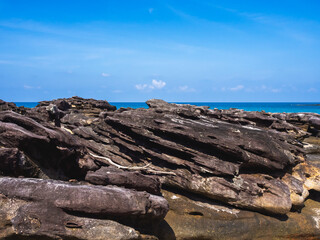 Summer background with piles of brown beach rocks in front of the tropical sea, skyline and open fresh blue sky on sunny day, vintage summer scene with nobody, holiday vacation poster concept.