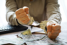 Hands Of A Fraudster With Handcuffs On A Background Of Us Dollars. Fraud, Cyber Crime Concept. Arrest Of An Entrepreneur In The Workplace.