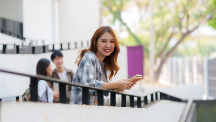 Wall Mural - Cute young Asian woman student standing holding a book outside in the university. Concept of learning and education in the university.