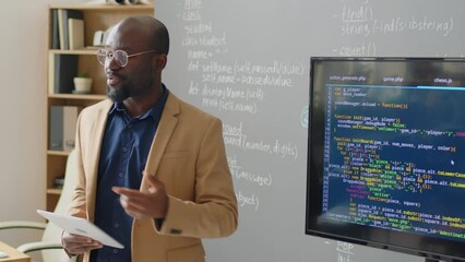 medium close up of male african american teacher standing in front of blackboard in classroom giving