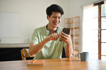 A happy Asian man is using his smartphone, scrolling on social media, chatting with his friends