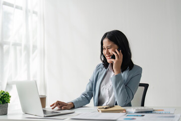 Sticker - Attractive young business woman talking on the mobile phone and smiling while sitting at her working place in office and at laptop