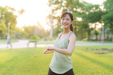 Wall Mural - Female jogger. Fit young Asian woman with green sportswear stretching muscle in park before running and enjoying a healthy outdoor. Fitness runner girl in public park. Wellness being concept