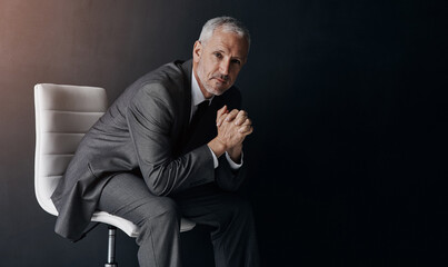 Aufkleber - Portrait, manager or corporate with a business man sitting on a chair in studio against a dark background. Leadership, management and a senior male CEO in a professional suit for his executive career